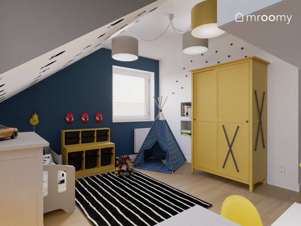 Żółte meble niebieska ściana czarny dywan w paski i namiot tipi w pokoju małego chłopaka