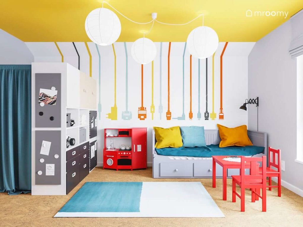 Pokój bawialnia dwóch chłopców z kolorową tapetą żółtym sufitem rozkładanym łóżkiem i czerwonym stoliczkiem