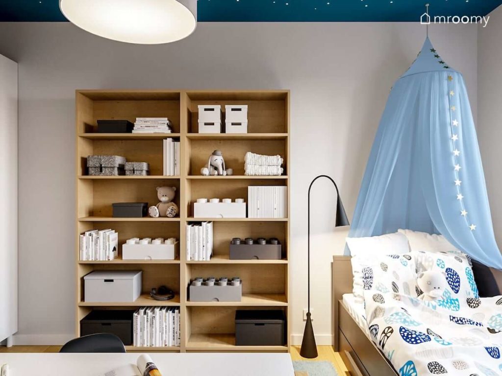 Regały na książki w kolorze jasnego drewna i łóżko z niebieskim baldachimem w pokoju dla dziewczynki