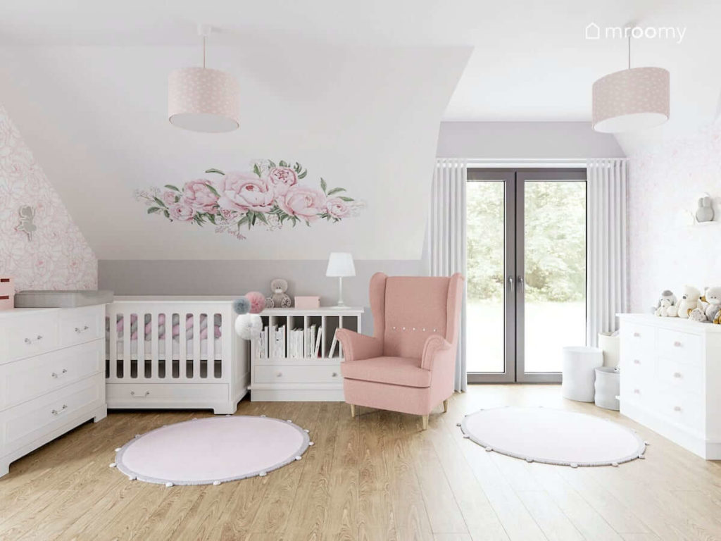Jasny poddaszowy pokój dla dziewczynki niemowlaka z białymi meblami różowym fotelem i naklejką w kwiaty na ścianie