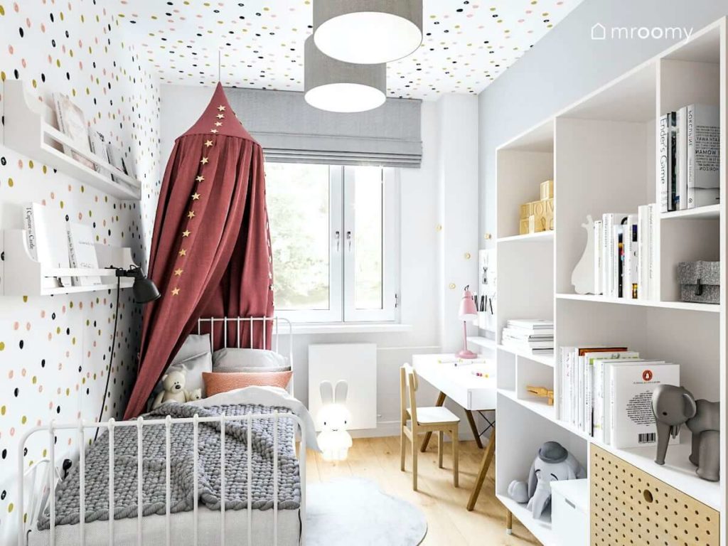 romantyczny pokój dla małej dziewczynki z mnóstwem zabawnych kropek na ścianie i suficie z metalowym łóżkiem z baldachimem białym regałem i biurkiem