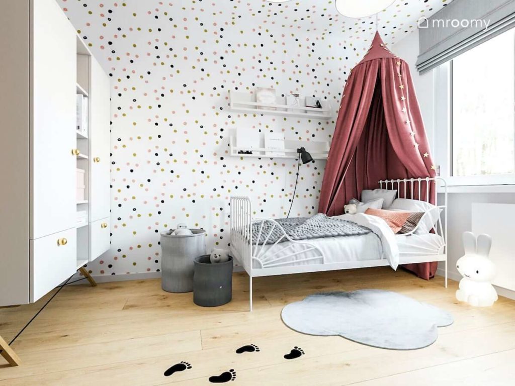 Metalowe białe łóżko z baldachimem dywan chmurka i ściana w kropki w pokoju małej dziewczynki