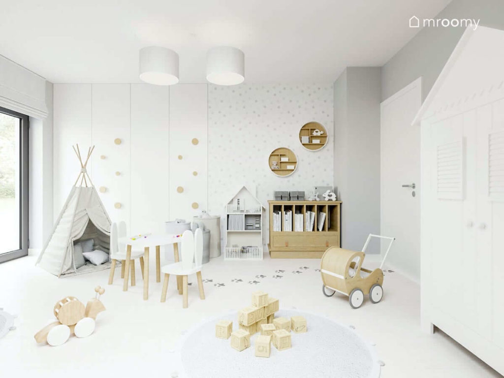 Jasny pokój małej dziewczynki z meblami z jasnego drewna okrągłymi uchwytami na białej szafie i szarym tipi