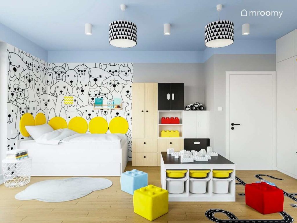 Łóżko w kącie z tapetą w pieski żółte okrągłe panele ścienne niebieski sufit i modułowe meble w pokoju chłopca