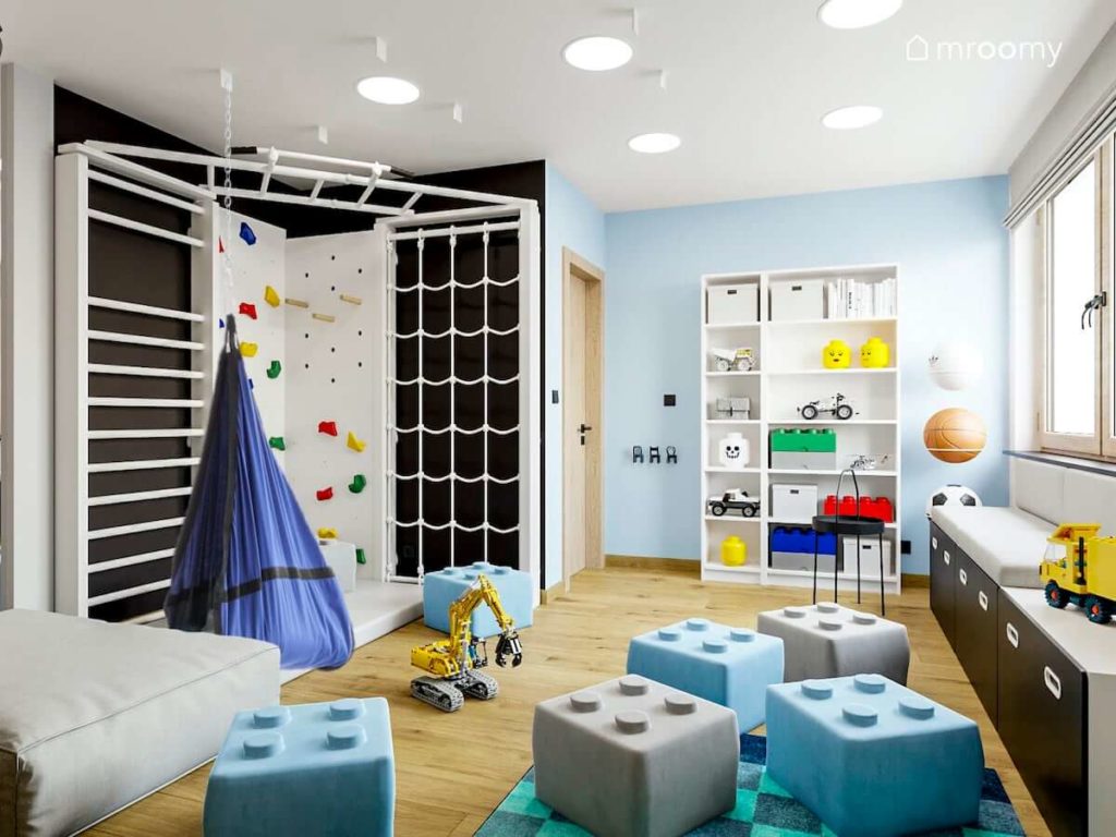 Kącik sportowy z białą  drabinką gimnastyczną i ścianką wspinaczkową pufy lego i niebieskie ściany w pokoju małego chłopca