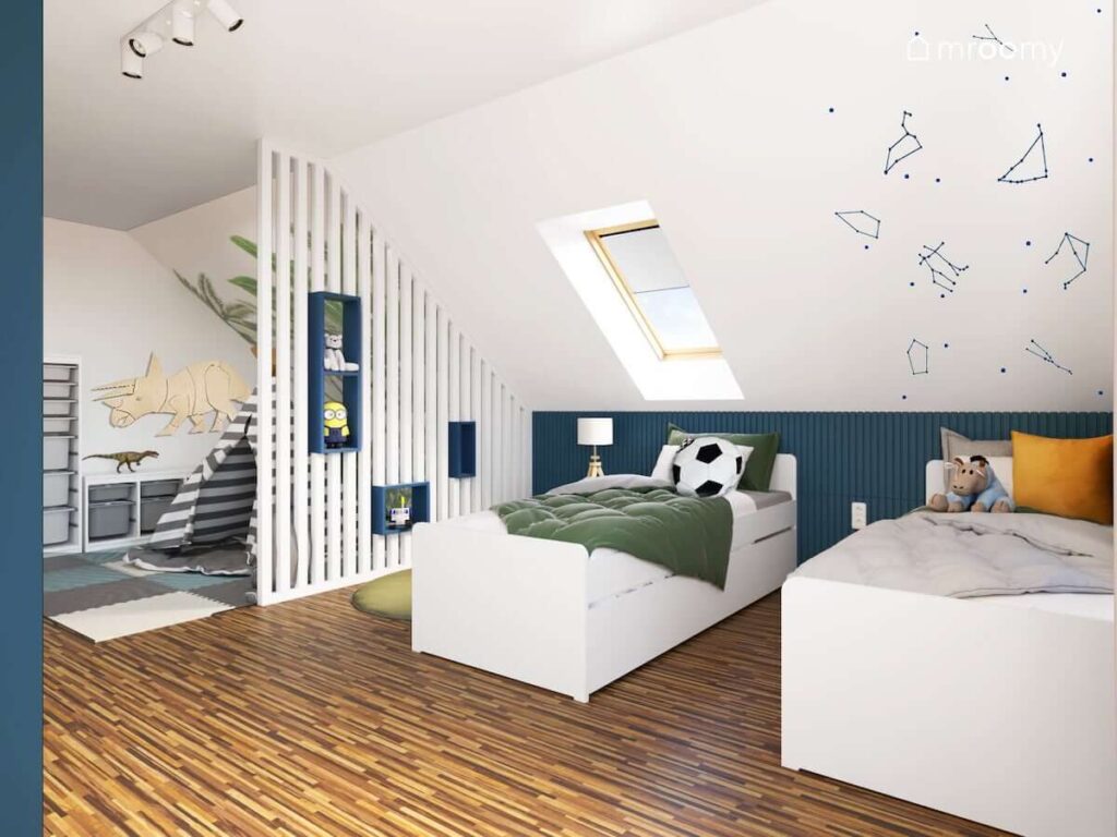 Strefa odpoczynku z dwoma białymi łóżkami oraz ścianą ozdobioną naklejkami z konstelacjami gwiazd w biało granatowym pokoju dwóch chłopców