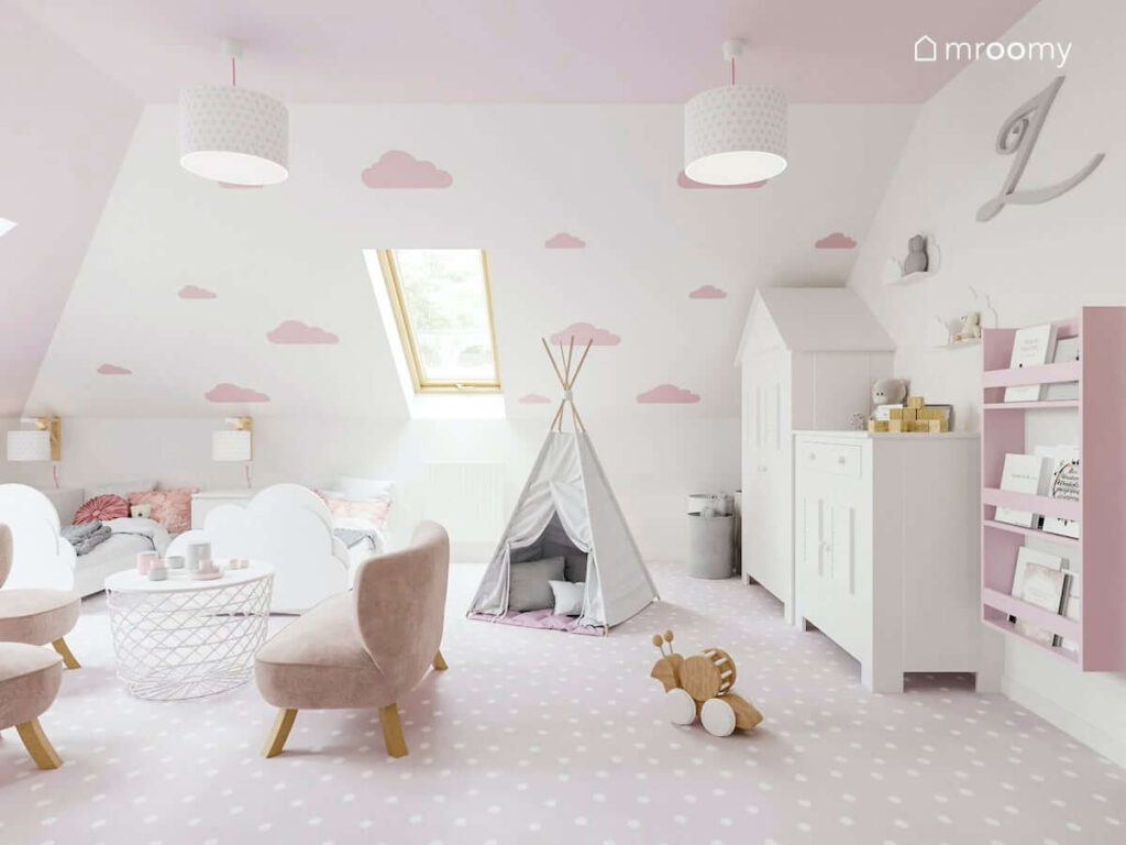 Dziewczęcy pokój dla bliźniaczek na poddaszu w kolorystyce biało-różowej z łóżkami w kształcie chmurki namiotem tipi jasnoróżową wykładziną na podłodze sofą i fotelikami dla dzieci stolikiem z miejscem do przechowywania