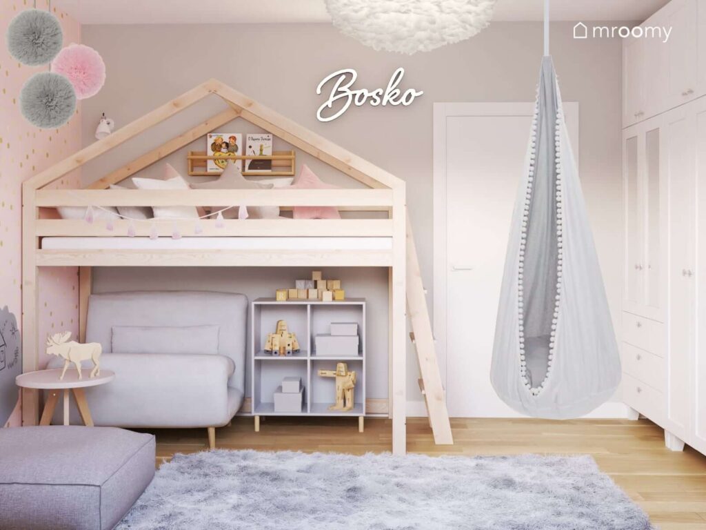 Drewniane łóżko w kształcie domku a pod nim rozkładana sofa i szafka na drewnianych nóżkach a także huśtawka kokon i ledon w kształcie napisu w pokoju dla kilkulatki dziewczynki