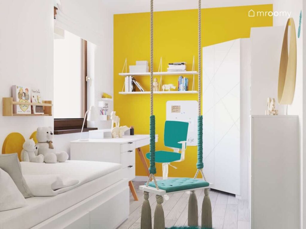 Biało żółty pokój dla dziewczynki z białym biurkiem łóżkiem półkami ściennymi i szafą oraz miętową huśtawką wiszącą i żółtą ścianą