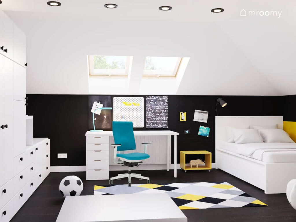 Biało czarny poddaszowy pokój dla chłopca w wieku szkolnym z białym biurkiem z organizerami i tablicami magnetycznymi a także białym łóżkiem i kolorowym dywanem