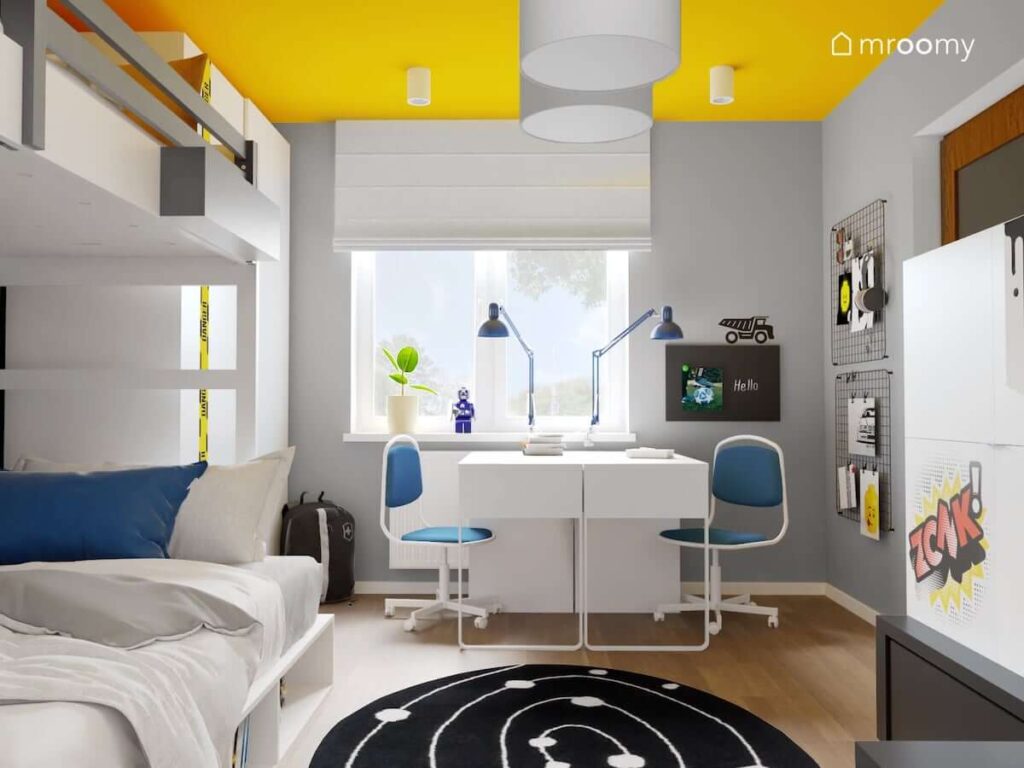 Szaro żółty pokój dla dwóch chłopców z dwoma biurkami z niebiesko białymi krzesłami oraz organizerami ściennymi i tablicą kredową