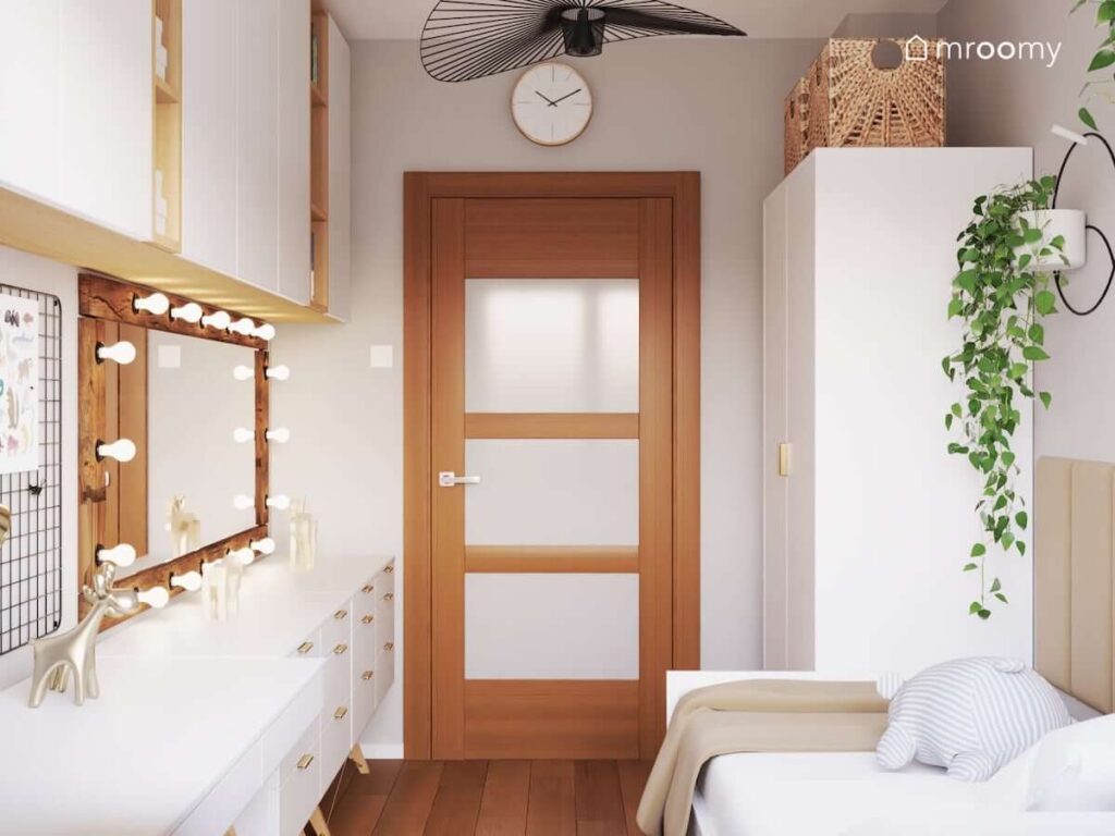 Przytulny pokój dla nastolatki utrzymany w ciepłych barwach a w nim białe meble lustro w drewnianej ramie z żarówkami oraz ozdobna lampa sufitowa