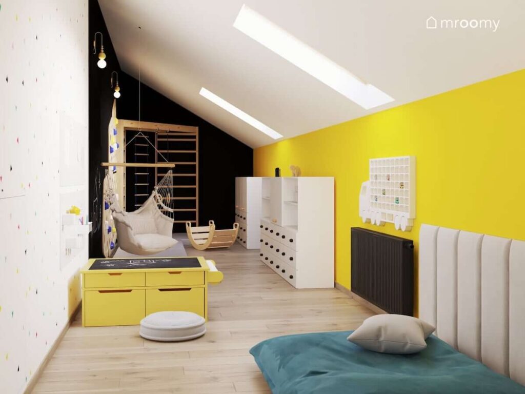Biało żółto czarny pokój zabaw dla rodzeństwa z licznymi szafkami stolikiem kreatywnym oraz ścianką wspinaczkową i drabinką narożną