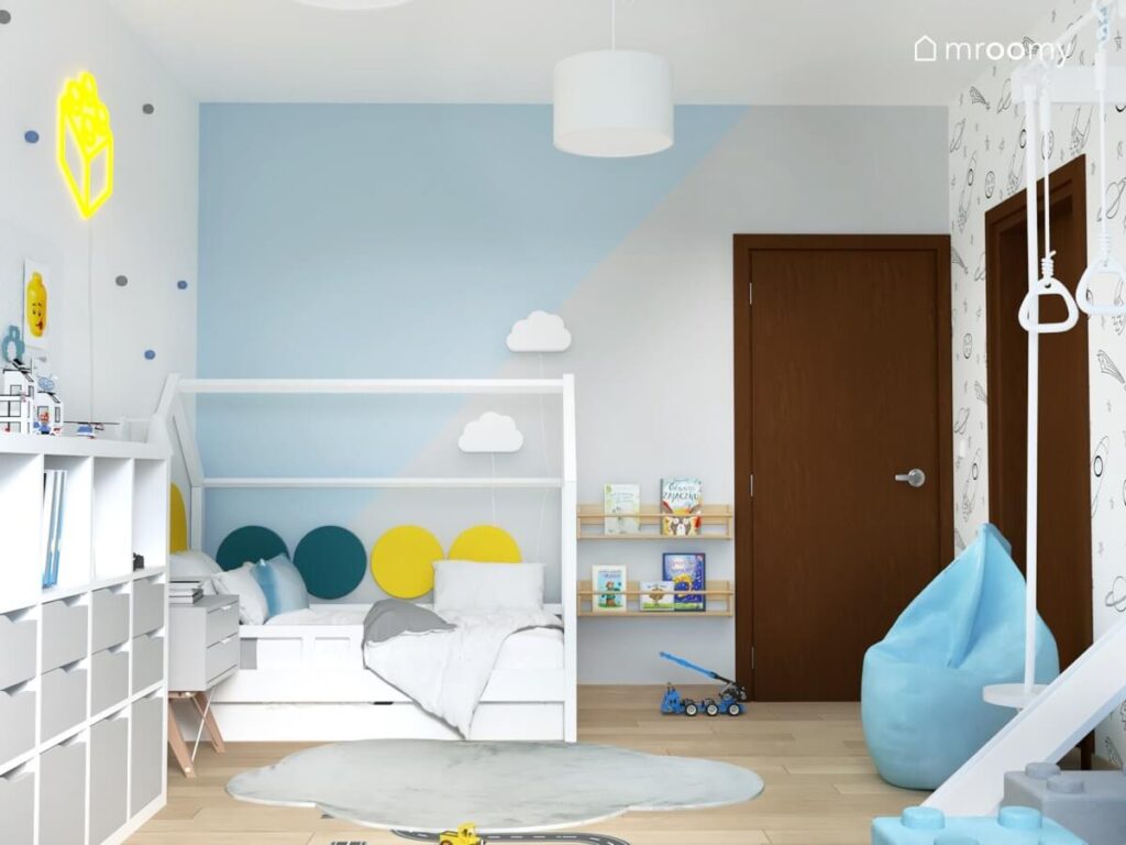 Biało szaro niebieski pokój dla chłopca a w nim białe łóżko domek uzupełnione niebieskimi i żółtymi panelami ściennymi i lampkami w kształcie chmurek