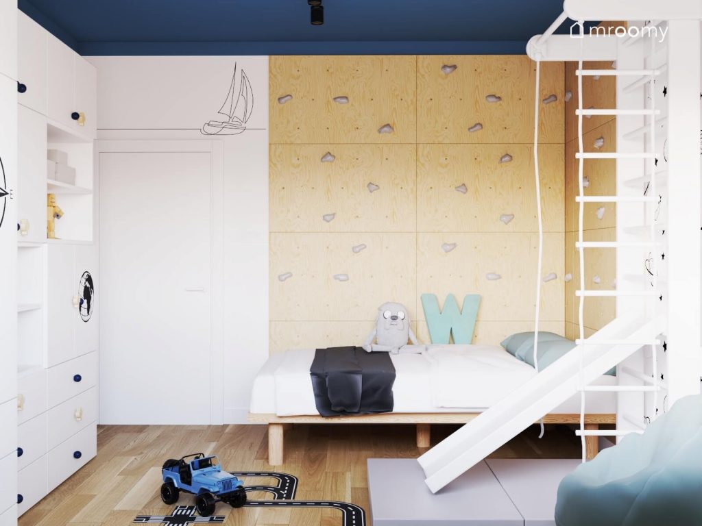 Duża ścianka wspinaczkowa ze sklejki drewniane łóżko oraz drabinka gimnastyczna ze zjeżdżalnią i materacem w biało niebieskim pokoju sześciolatka