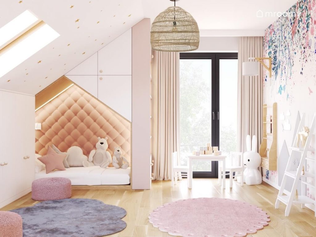 Jasny poddaszowy pokój dla dwóch dziewczynek ze skosem ozdobionym złotymi gwiazdkami dwoma różowymi pufami szarym i różowym dywanem oraz łóżkiem-domkiem