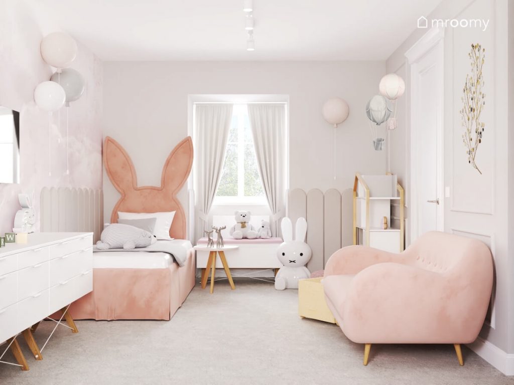 Jasny pokój dla dziewczynki z różową kanapą różowym tapicerowanym łóżkiem z zagłówkiem w kształcie królika oraz z dodatkami w kształcie balonów