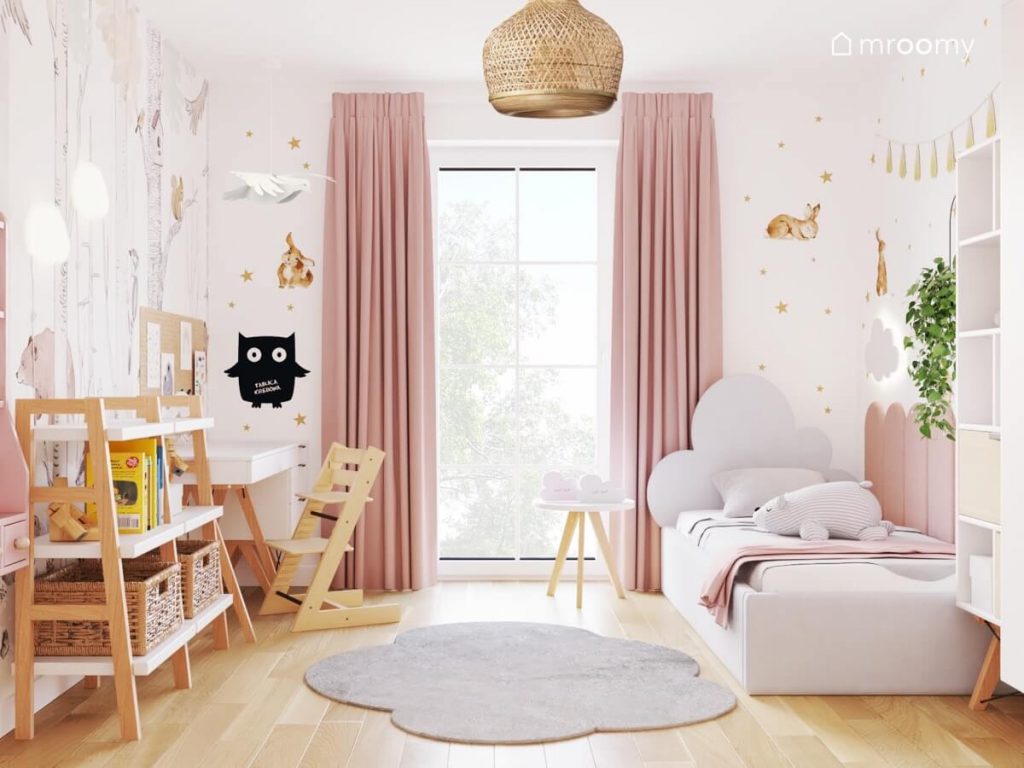 Biały pokój dla dziewczynki z biało drewnianymi meblami szarym łóżkiem z zagłówkiem w kształcie chmurki różowymi zasłonami oraz ścianami ozdobionymi złotymi gwiazdkami i naklejkami w kształcie królików