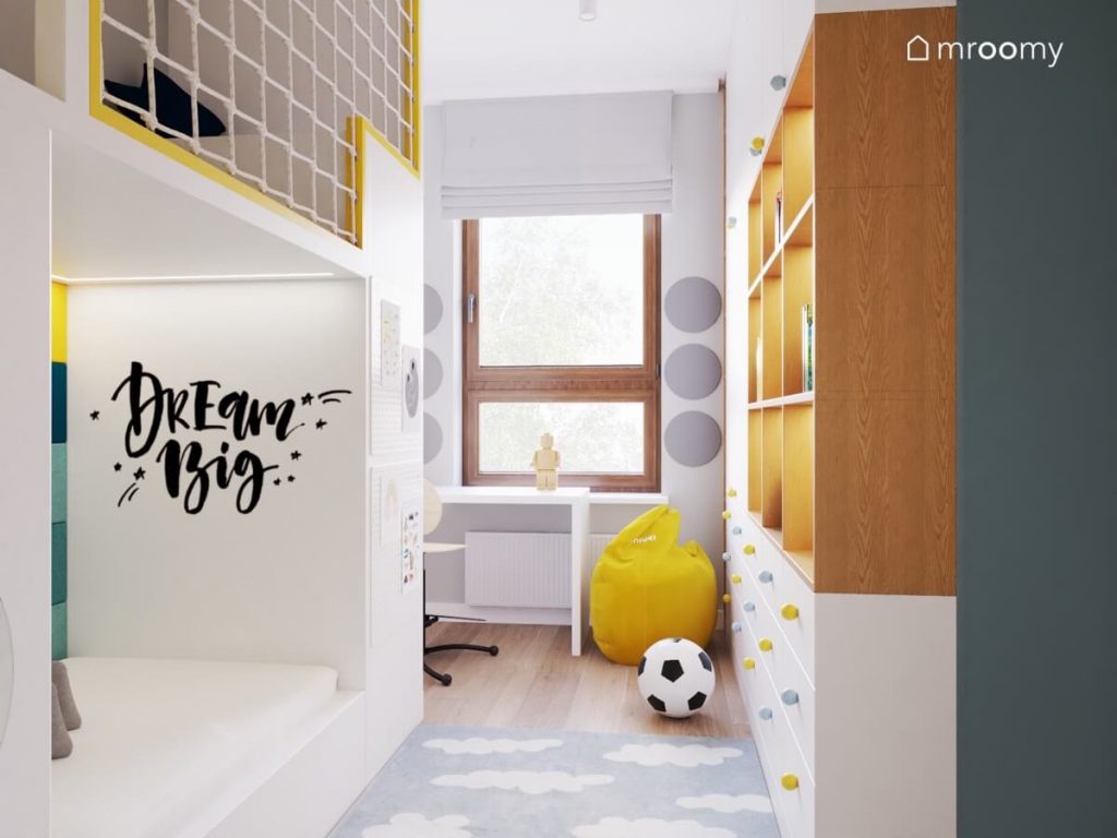 Jasny pokój kilkuletniego chłopca a w nim antresola z miejscem do spania i do zabawy biała szafa z drewnianymi elementami białe biurko żółta pufa oraz dywan w chmurki