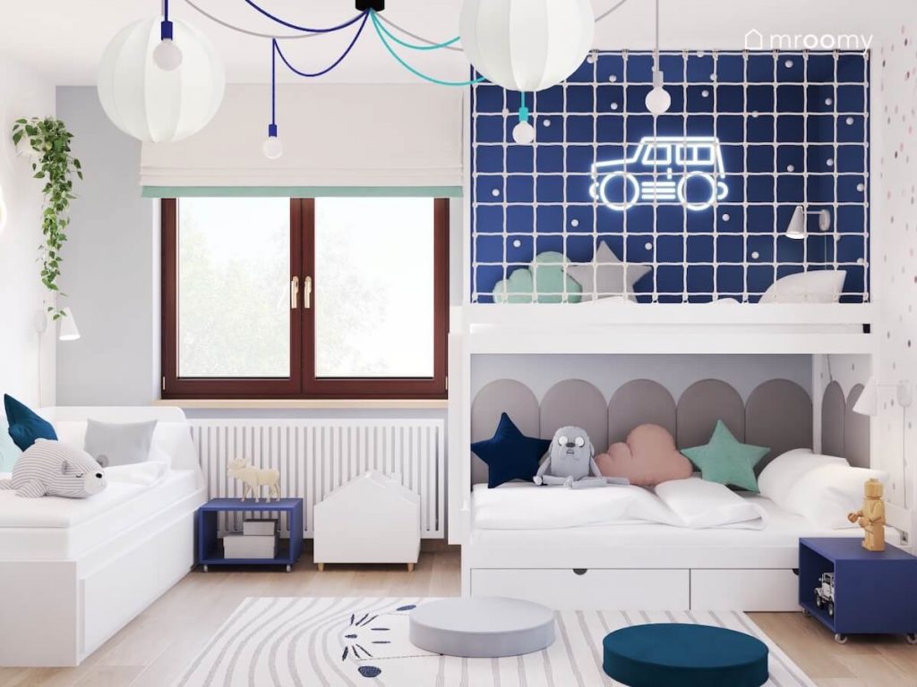 Sypialnia rodzeństwa a w niej dwa łóżka ciemnoniebieska antresola płaskie pufki oraz lampy na kolorowym okablowaniu