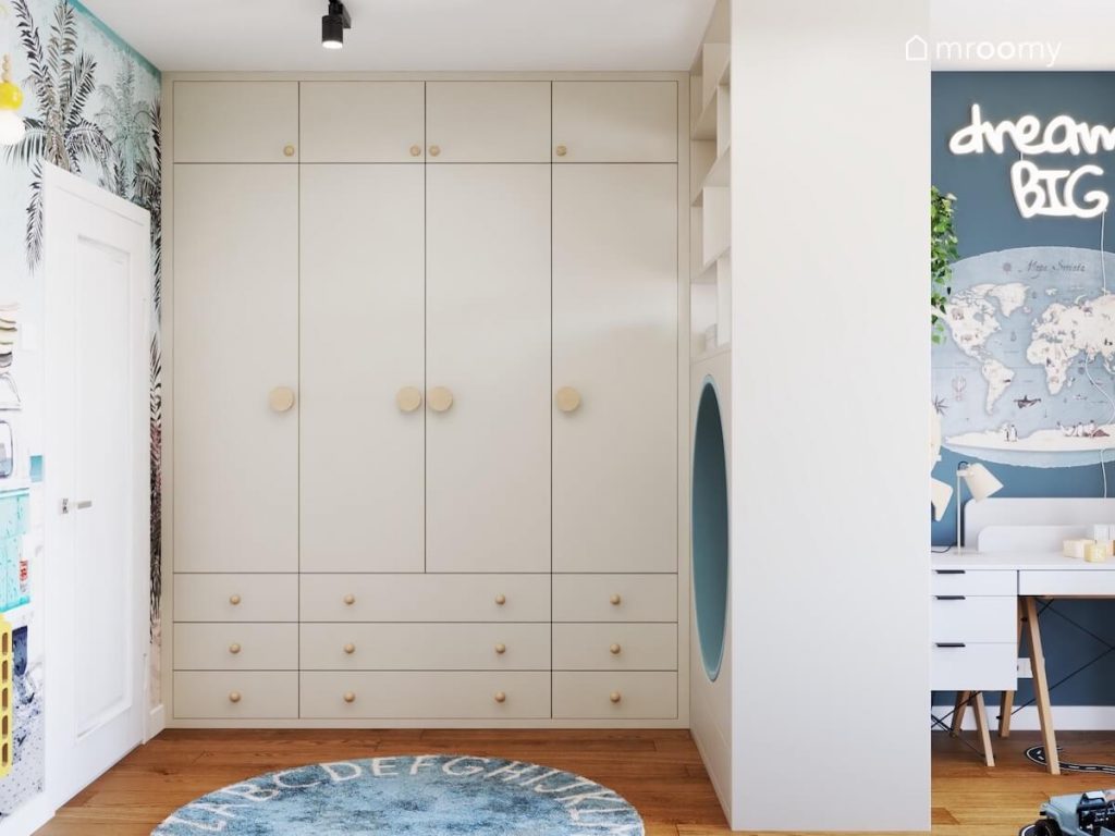 Duża kremowa szafa z drewnianymi uchwytami a na podłodze niebieski dywan z alfabetem w pokoju dla chłopca