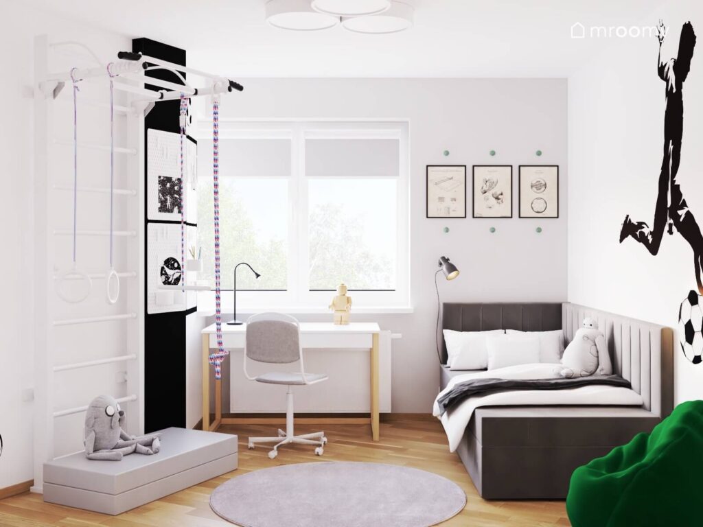 Biało szary pokój dla chłopca w wieku szkolnym a w nim ciemnoszare łóżko biało drewniane biurko drabinka gimnastyczna organizery ścienne i plakaty