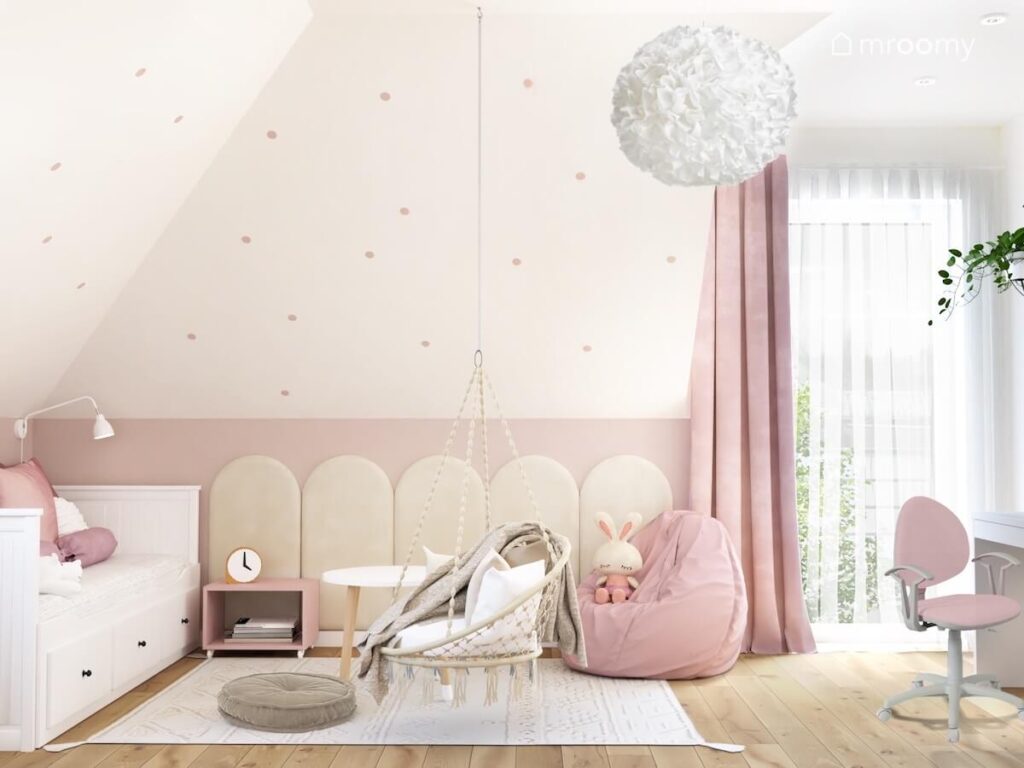 Strefa spania i odpoczynku w poddaszowym pokoju dziewczynki a w niej białe łózko fotel wiszący i różowy worek do siedzenia oraz duży dywan i panele ścienne