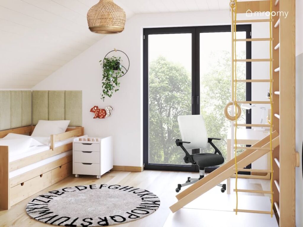 Jasny poddaszowy pokój dla chłopca a w nim drewniane łóżko uzupełnione zielonymi panelami drabinka gimnastyczna ze zjeżdżalnią kwietnik oraz dywan z alfabetem