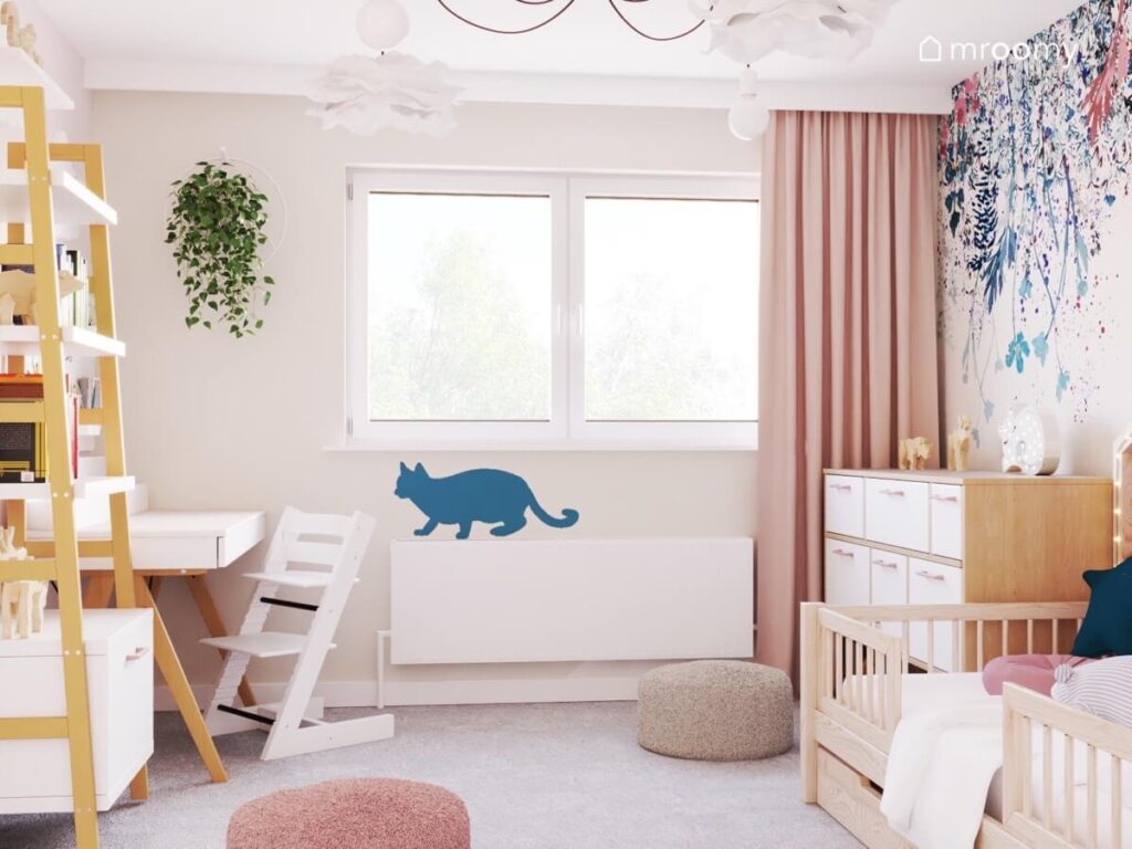 Przytulny pokój dla dziewczynki z białymi i drewnianymi meblami ozdobnym kwietnikiem pufkami i naklejką kotem