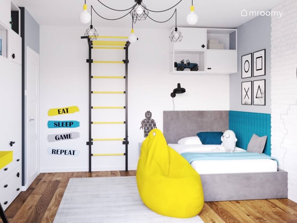 Jasny pokój dla nastolatka a w nim szare łóżko żółta pufa czarno żółta drabinka gimnastyczna oraz gamingowe dodatki