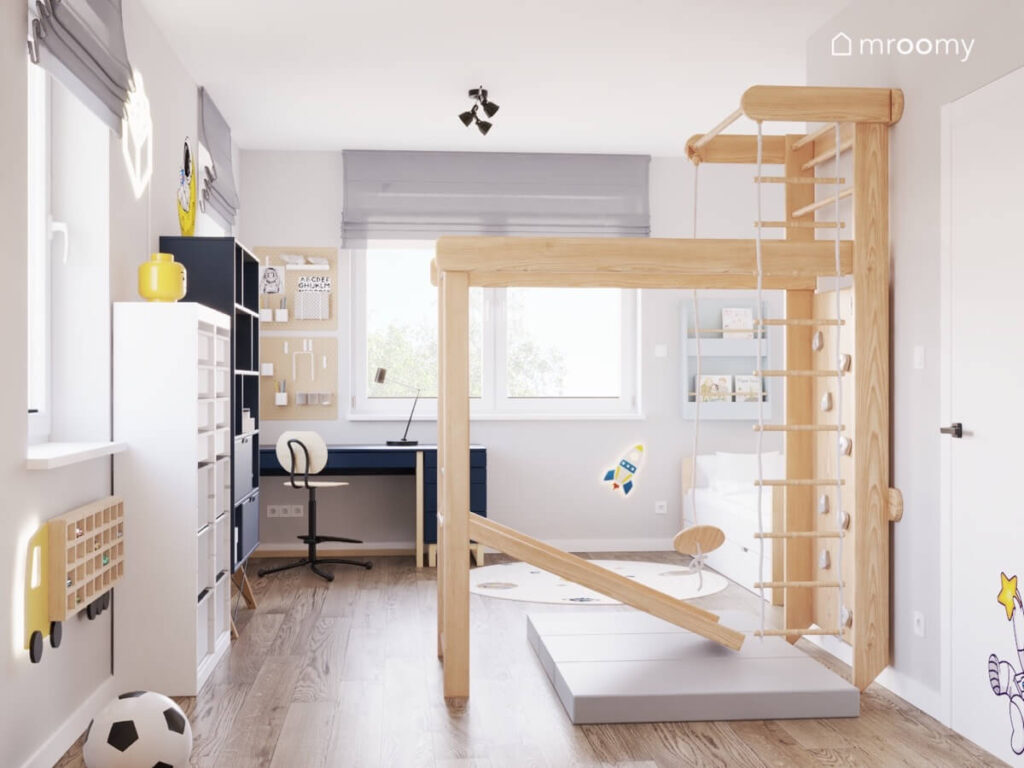 Jasny pokój dla chłopca w wieku szkolnym a w nim drewniany plac zabaw oraz białe i granatowe meble