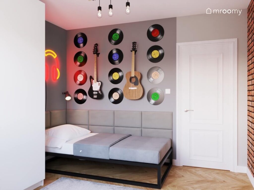 Proste metalowe łóżko uzupełnione miękkimi panelami a nad nim płyty winylowe oraz gitary w pokoju dla nastolatka miłośnika muzyki