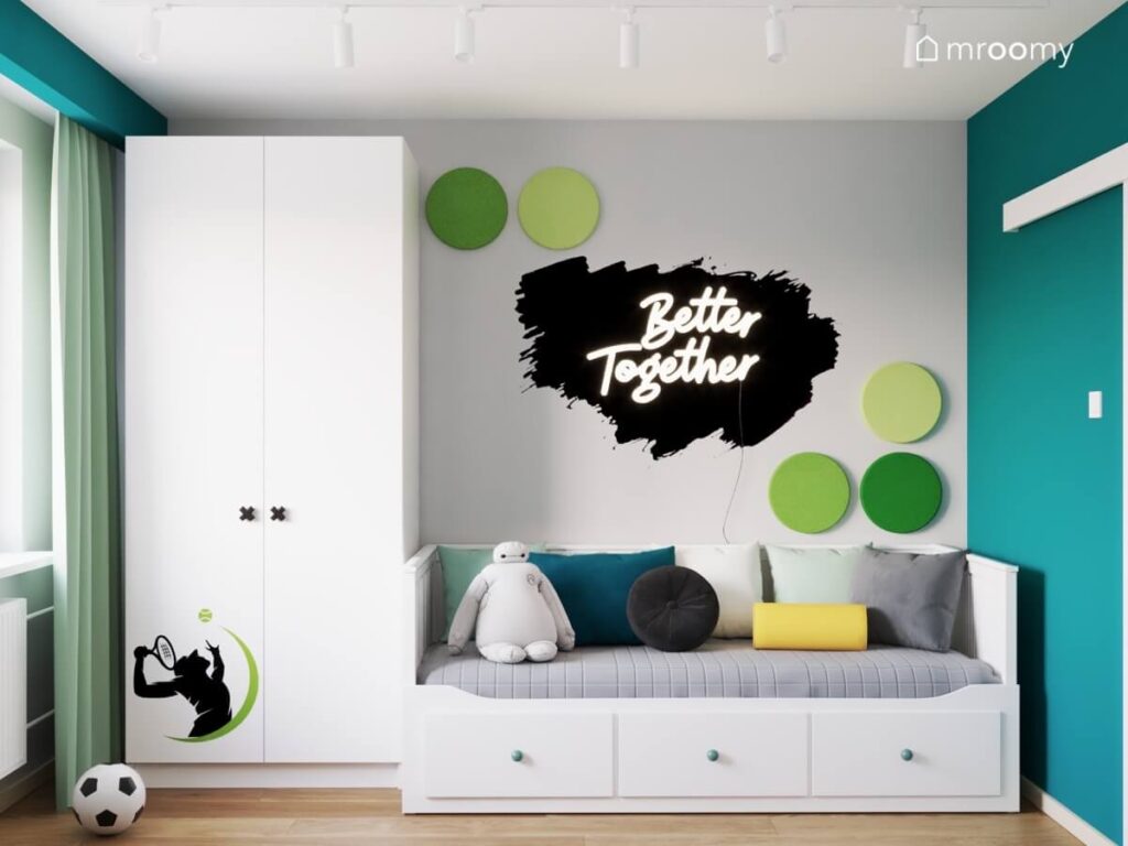 Biała szafa z naklejką z tenisistą a obok łóżko z szufladami a na ścianie ledon w kształcie napisu i zielone panele ścienne w szaro zielono białym pokoju dwóch chłopców