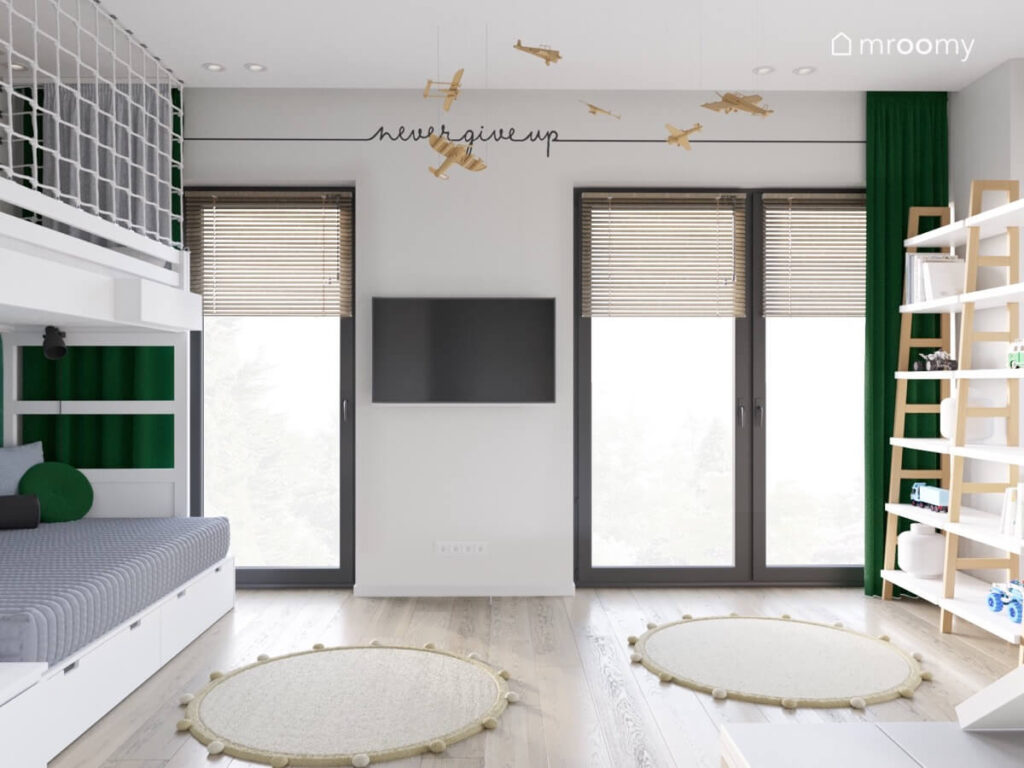Jasny pokój dla chłopca z zielonymi zasłonami drewnianymi samolotami u sufitu beżowymi dywanami oraz naklejką Never give up na ścianie