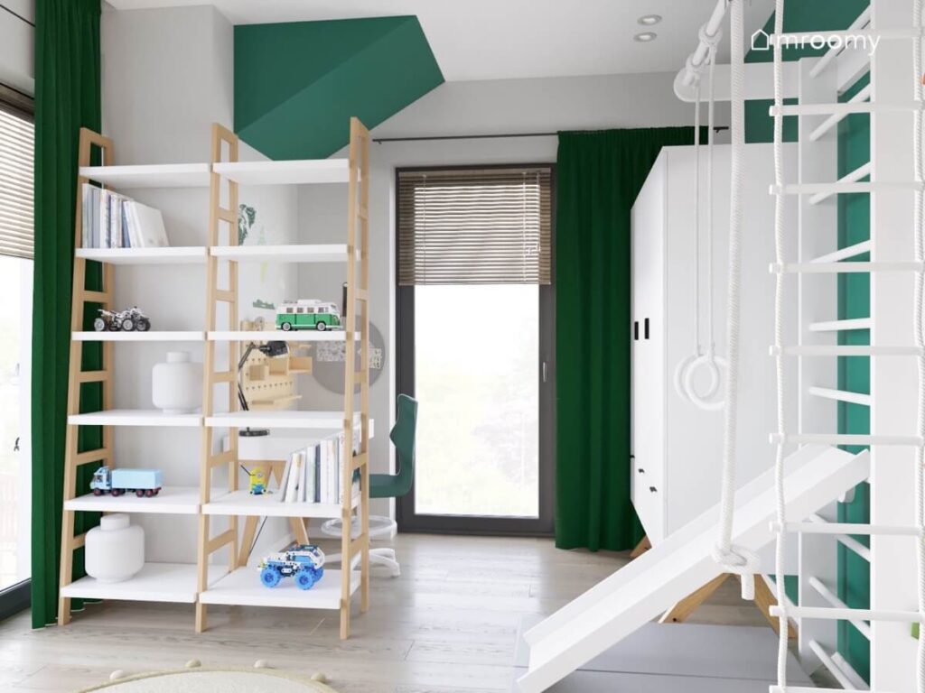 Szaro zielony pokój dla chłopca a w nim biało drewniany regał biała szafa zielone zasłony oraz drabinka gimnastyczna ze zjeżdżalnią
