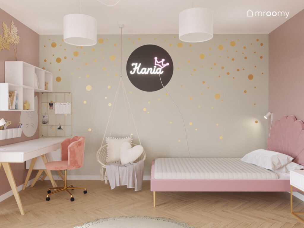 Beżowa ściana w pokoju dziewczynki a na niej złote kropki i ledon a przed nią fotel wiszący i różowe łóżko