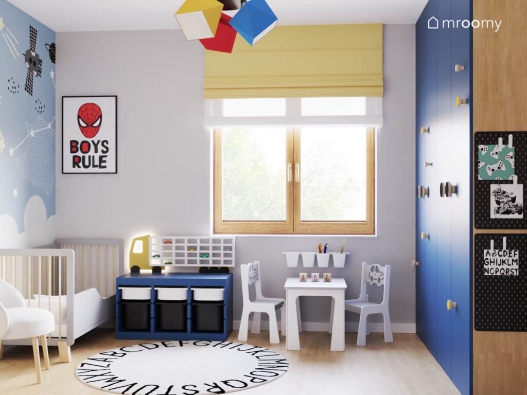 Plakat ze Spidermanem drewniane łóżeczko dla dziecka dywan z alfabetem oraz duża niebieska szafa w pokoju dwóch chłopców
