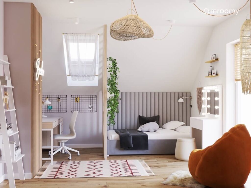 Jasny poddaszowy pokój dla nastolatki a w nim szare tapicerowane łóżko uzupełnione panelami ściennymi na podłodze wzorzysty dywan a na suficie bambusowa lampa