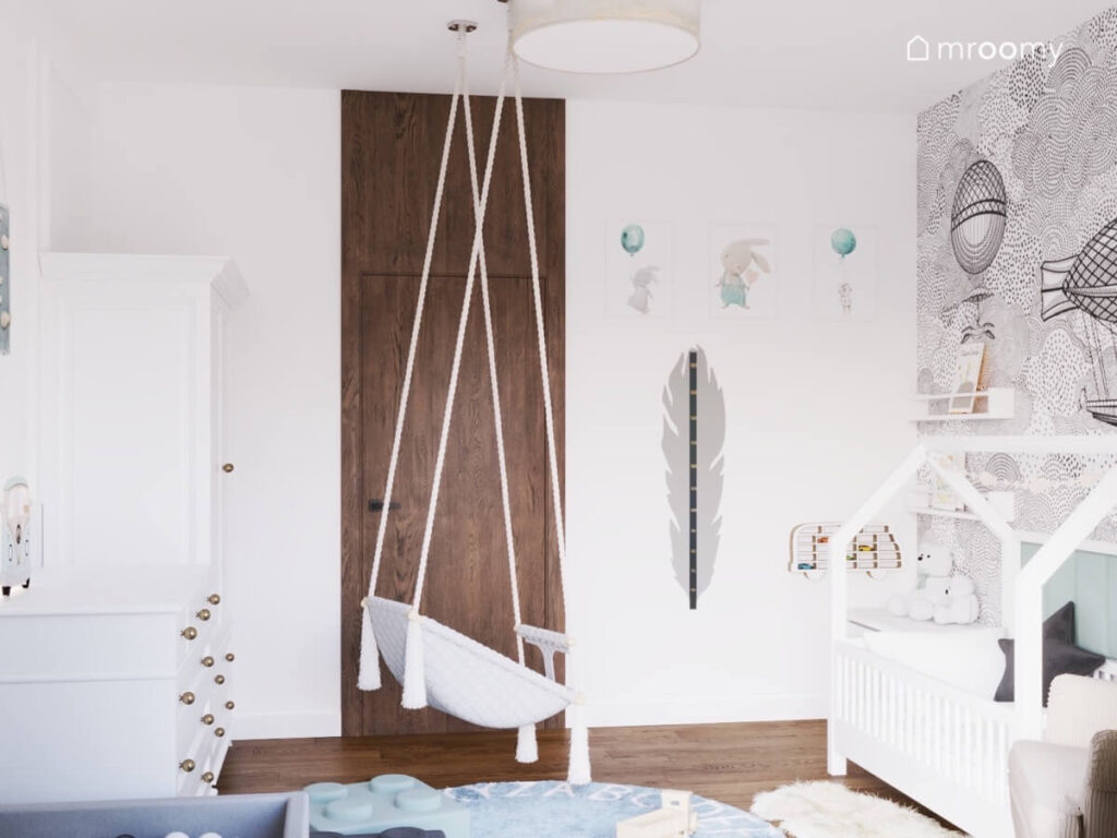 Biały pokój dla malutkiego chłopca a w nim łóżko domek fotel wiszący oraz liczne ozdoby na ścianach