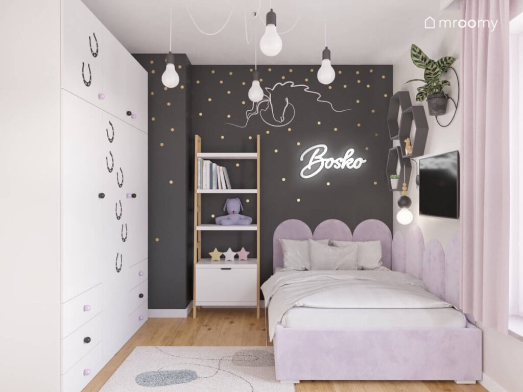 Biało czarny pokój dla dziewczynki w wieku szkolnym z dużą białą szafą jasnofioletowym tapicerowanym łóżkiem regałem oraz złotymi kropkami i ledonem na ścianie