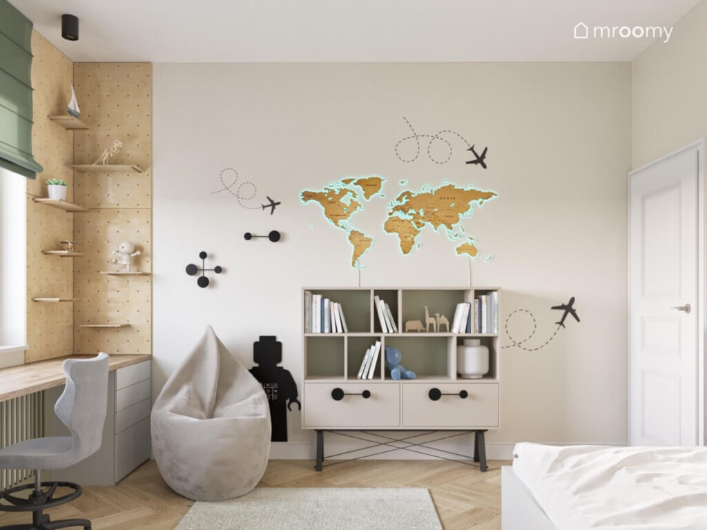 Beżowa ściana w pokoju chłopca a na niej drewniana mapa świata komoda naklejki samoloty tablica kredowa w kształcie ludzika oraz uchwyty w ciekawych kształtach