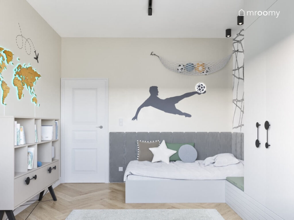 Jasny pokój dla chłopca z prostym łóżkiem uzupełnionym szarymi panelami ściennymi oraz piłkarskimi naklejkami na ścianach