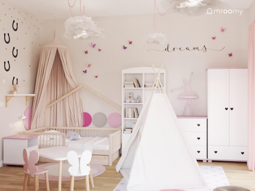 Beżowy pokój dla dziewczynki a w nim drewniane łóżko z baldachimem namiot tipi oraz białe meble a na ścianie motylki