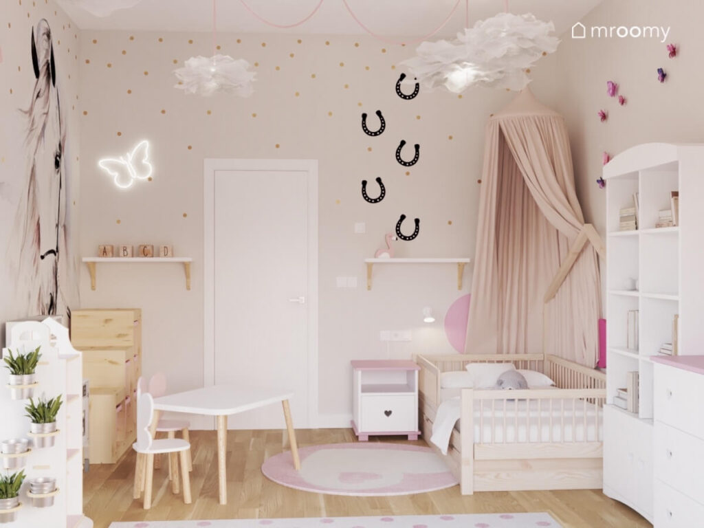 Jasny pokój dla dziewczynki z drewnianym łóżkiem uzupełnionym baldachimem naklejkami w kształcie podków na ścianie i ledonem motyl