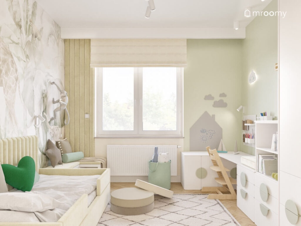 Jasnozielony pokój dla małego chłopca z białymi szafkami tapicerowanym łóżkiem niskimi pufkami oraz tablicą kredową